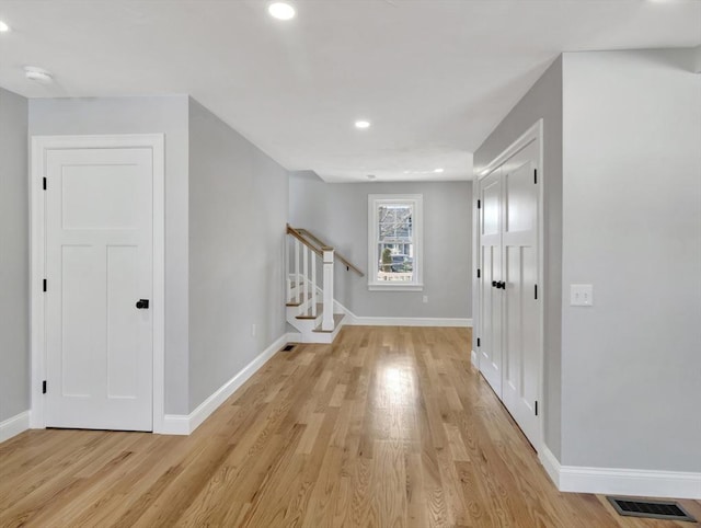 corridor featuring stairs, light wood-style floors, visible vents, and baseboards