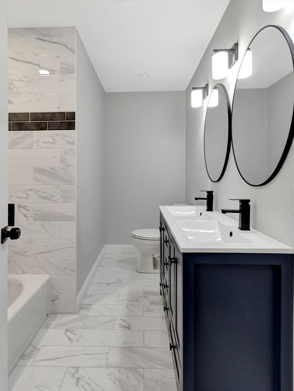 bathroom with baseboards, double vanity, a sink, toilet, and marble finish floor