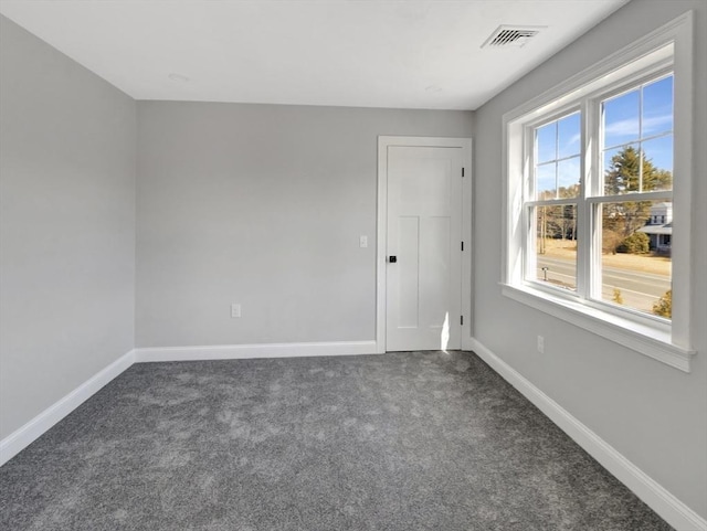 spare room with dark colored carpet, visible vents, and baseboards