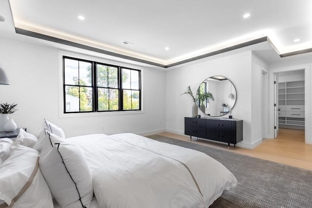 bedroom with a spacious closet, a tray ceiling, and light hardwood / wood-style floors