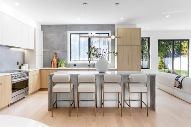 kitchen with a center island, a breakfast bar, light wood-type flooring, stainless steel electric range oven, and white cabinets