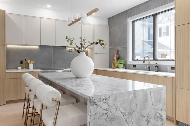 kitchen featuring white cabinetry, a kitchen bar, a center island, light stone countertops, and sink