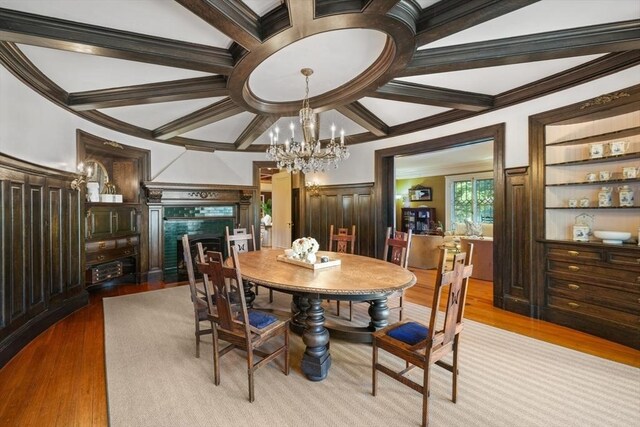 dining space with coffered ceiling, wood finished floors, a chandelier, crown molding, and a fireplace with flush hearth