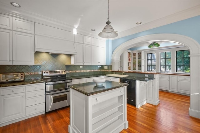 kitchen featuring range with two ovens, dishwasher, a sink, arched walkways, and premium range hood