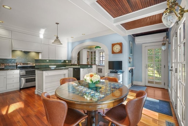 dining room with arched walkways, wood finished floors, recessed lighting, and beam ceiling
