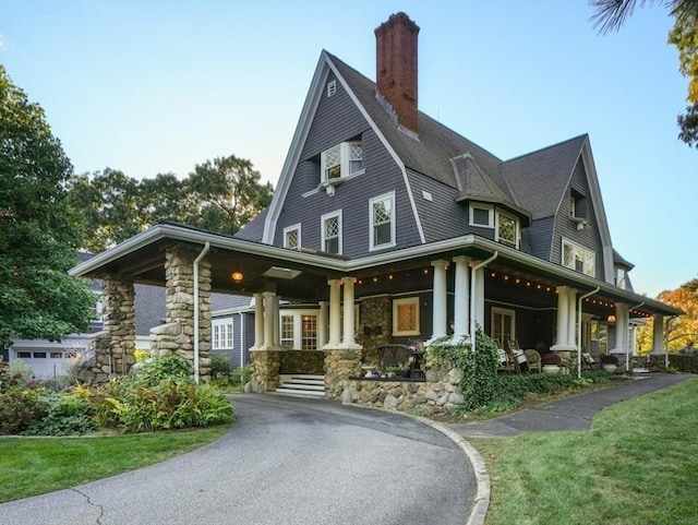rear view of property with covered porch, a chimney, a yard, and stone siding