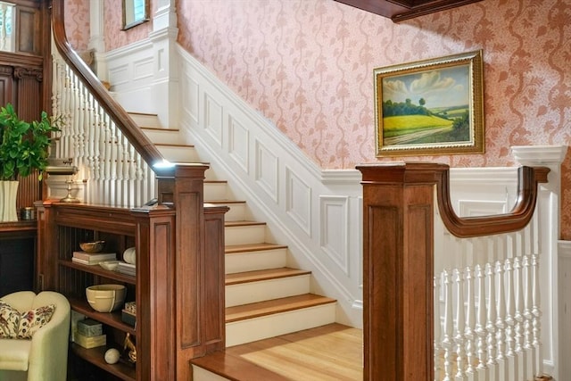 stairs with wallpapered walls, a wainscoted wall, and wood finished floors