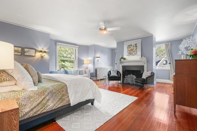 bedroom featuring wood finished floors, a fireplace, and ceiling fan
