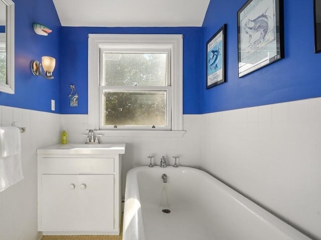 bathroom featuring a freestanding bath, wainscoting, vanity, and tile walls