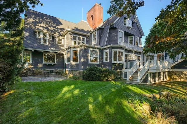 rear view of house with a chimney, a yard, a patio, a balcony, and stairway