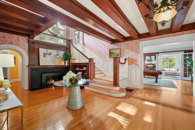 entrance foyer featuring wallpapered walls, hardwood / wood-style flooring, stairs, beam ceiling, and wainscoting
