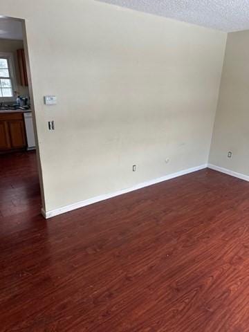 empty room with a textured ceiling, dark wood-type flooring, and baseboards