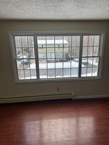 spare room featuring a wealth of natural light, a baseboard radiator, baseboards, and dark wood-style flooring