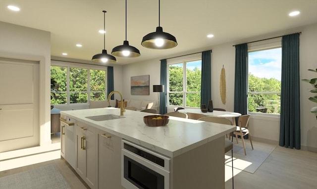 kitchen with sink, light stone counters, plenty of natural light, a kitchen island with sink, and white cabinets