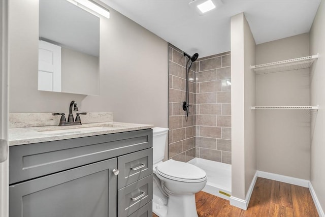 bathroom featuring a tile shower, hardwood / wood-style floors, vanity, and toilet