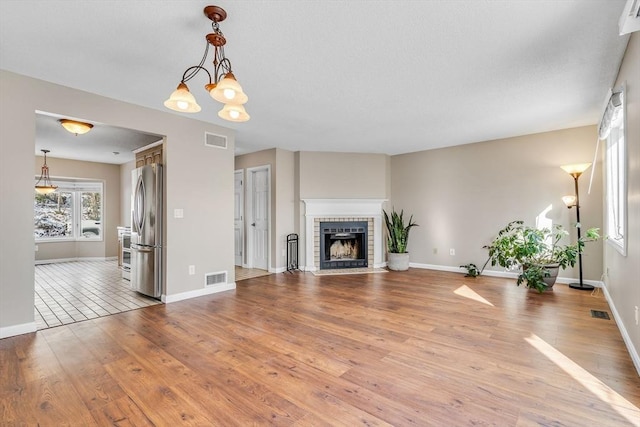 unfurnished living room featuring an inviting chandelier, a fireplace, and light hardwood / wood-style floors