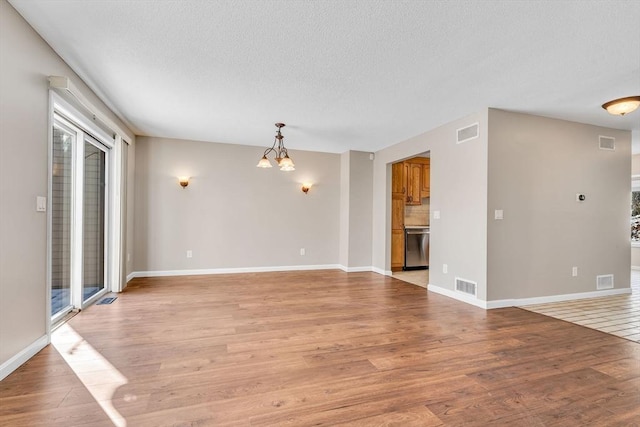 unfurnished living room featuring a textured ceiling, light hardwood / wood-style flooring, and a notable chandelier