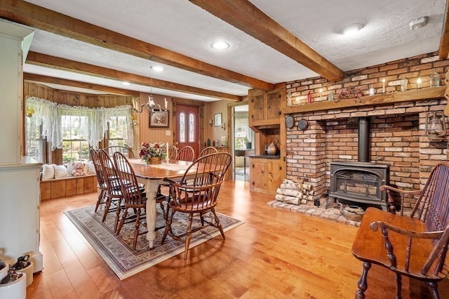 dining area featuring beam ceiling, light wood-type flooring, a textured ceiling, and a wood stove