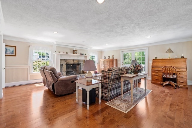 living room with a textured ceiling, crown molding, a fireplace, and wood-type flooring