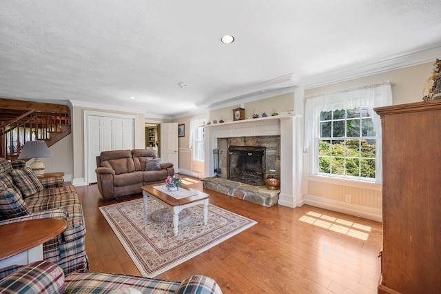 living room with hardwood / wood-style floors, a stone fireplace, crown molding, and a textured ceiling