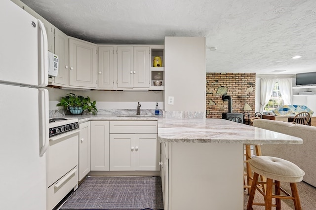 kitchen featuring white cabinetry, a kitchen bar, a wood stove, sink, and white appliances