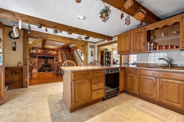 kitchen featuring black dishwasher, light tile patterned flooring, sink, a wood stove, and kitchen peninsula