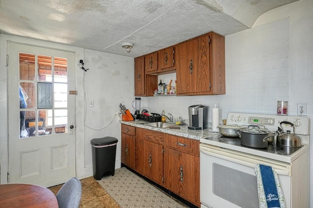 kitchen with brown cabinets, white range with electric cooktop, a sink, a textured ceiling, and light countertops