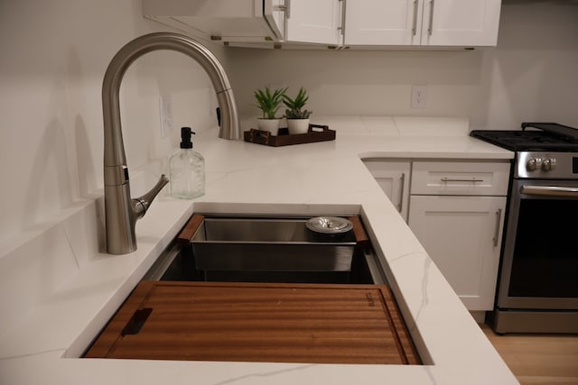 kitchen with sink, stainless steel range, hardwood / wood-style flooring, and white cabinets