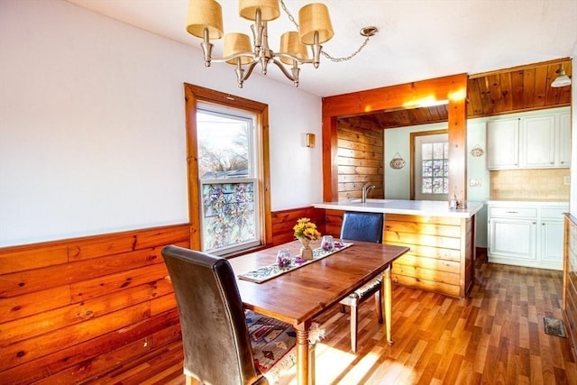 dining area with beam ceiling, dark wood-type flooring, a notable chandelier, and wood walls