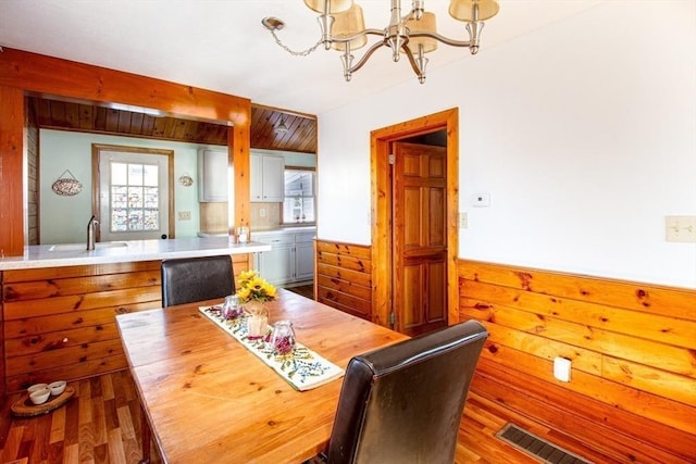 dining area featuring light hardwood / wood-style flooring, wood walls, sink, and a chandelier