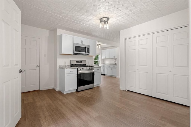 50 Howard St, Haverhill, MA 01830 - kitchen with stainless steel appliances, white cabinets, light wood-style floors, light stone countertops, and an ornate ceiling