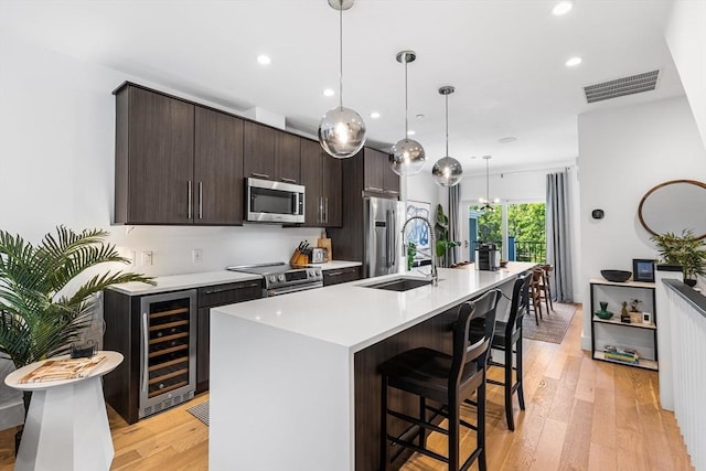 kitchen with appliances with stainless steel finishes, beverage cooler, dark brown cabinets, a sink, and a kitchen breakfast bar