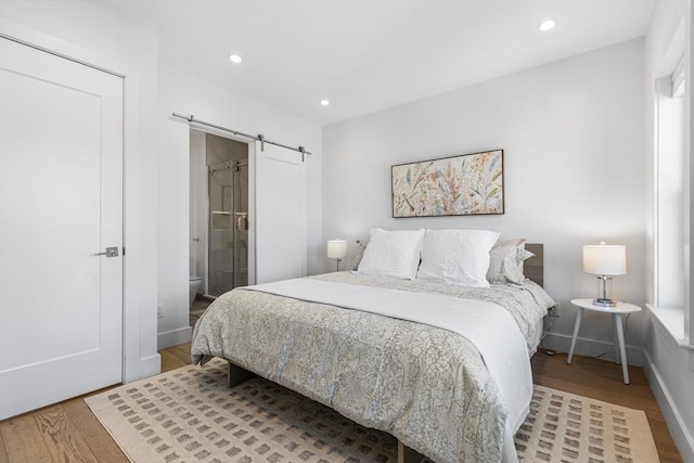 bedroom with a barn door, wood finished floors, recessed lighting, and baseboards