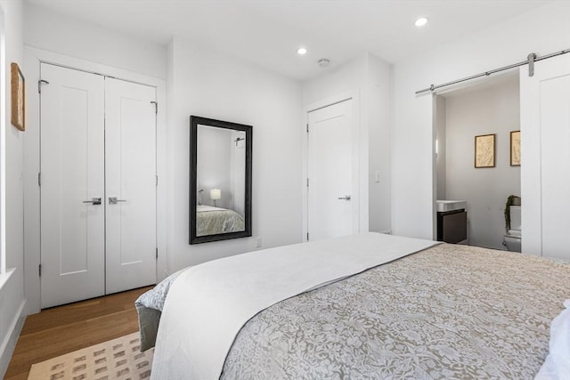 bedroom with wood finished floors, a barn door, recessed lighting, and a closet