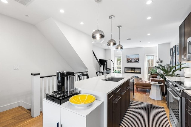kitchen with a sink, stainless steel appliances, light wood-type flooring, light countertops, and dark brown cabinets