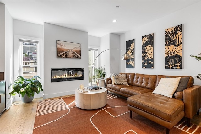 living area with a glass covered fireplace, wood finished floors, recessed lighting, and baseboards
