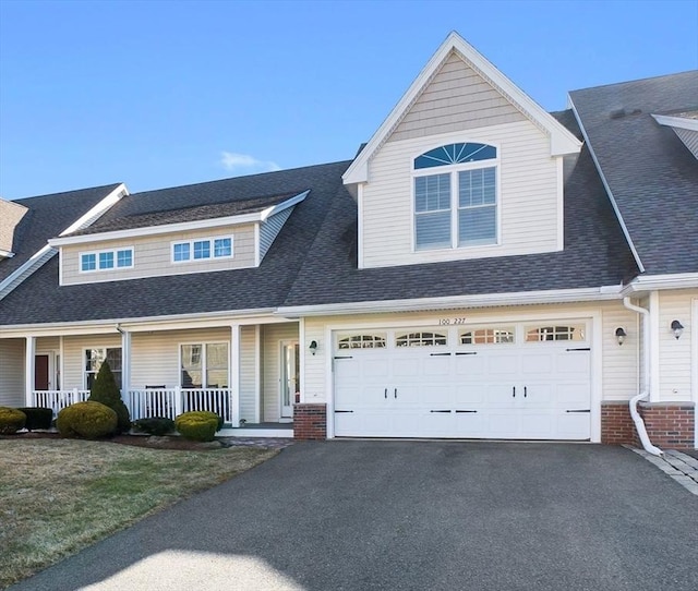 multi unit property featuring aphalt driveway, covered porch, a shingled roof, a garage, and brick siding