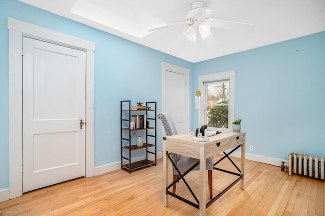 home office featuring light hardwood / wood-style floors, radiator, a skylight, and ceiling fan