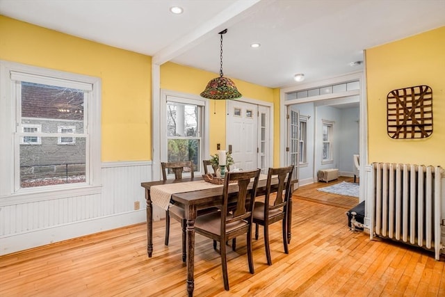 dining area featuring radiator heating unit, beam ceiling, and light hardwood / wood-style flooring