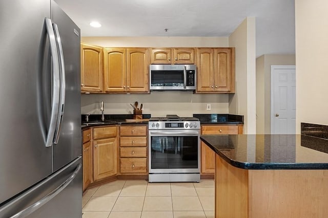 kitchen featuring stainless steel appliances, sink, light tile patterned floors, and dark stone counters