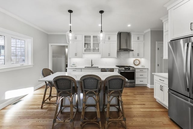 kitchen featuring appliances with stainless steel finishes, a breakfast bar, wall chimney exhaust hood, and crown molding
