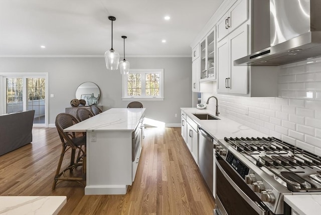 kitchen with crown molding, appliances with stainless steel finishes, a kitchen breakfast bar, wall chimney exhaust hood, and a sink
