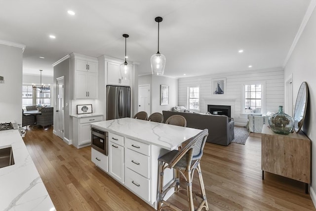 kitchen featuring crown molding, a breakfast bar area, white cabinets, a fireplace, and stainless steel fridge