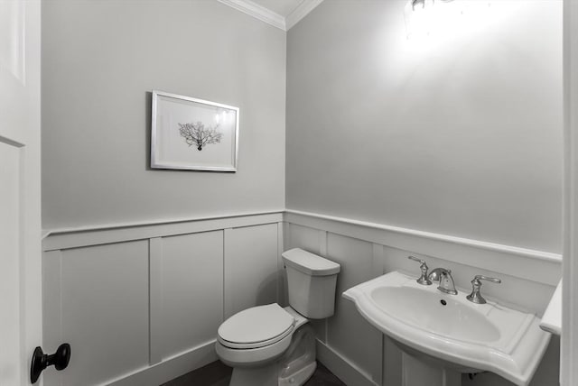 half bath with a sink, a wainscoted wall, toilet, and ornamental molding
