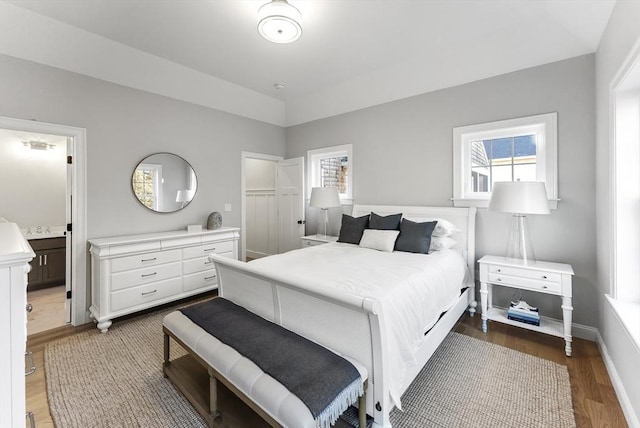 bedroom featuring wood finished floors, baseboards, and ensuite bathroom