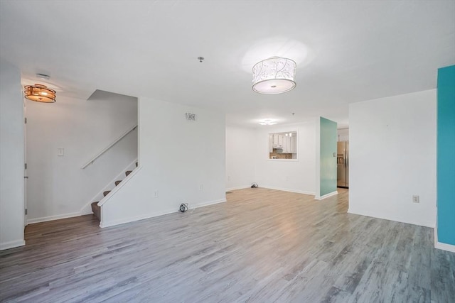 unfurnished living room featuring baseboards, light wood finished floors, and stairway