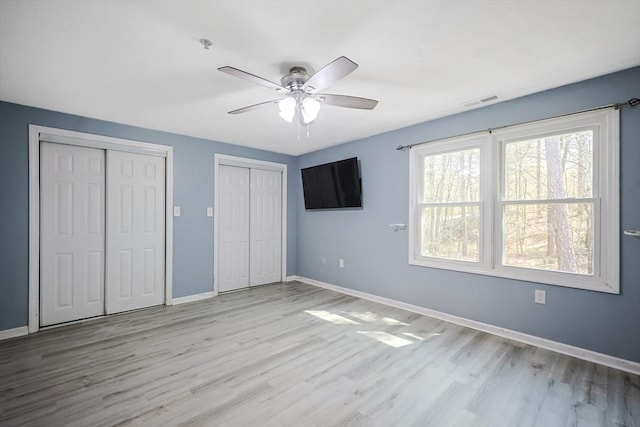 unfurnished bedroom featuring baseboards, two closets, visible vents, and wood finished floors