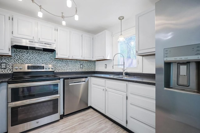 kitchen with dark countertops, under cabinet range hood, white cabinets, a sink, and stainless steel appliances