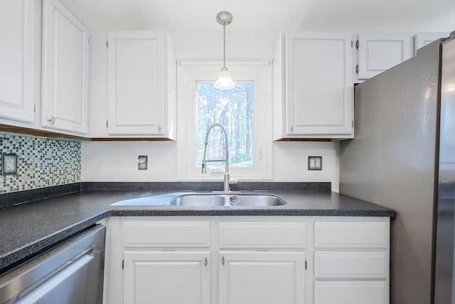 kitchen featuring white cabinets, dark countertops, hanging light fixtures, appliances with stainless steel finishes, and a sink