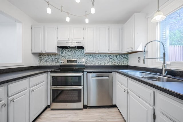 kitchen featuring white cabinets, dark countertops, a sink, stainless steel appliances, and under cabinet range hood